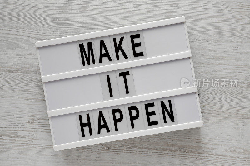 白色木质背景上写着“Make it happen”的灯箱，俯视图。从上面，平躺在头顶上。